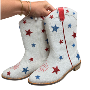 White glittery boots with red and blue star patterns held by a hand on a white background
