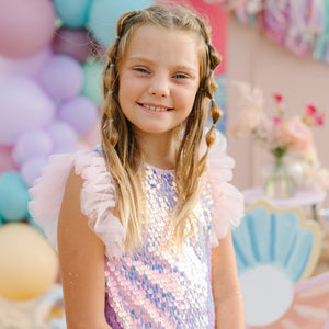 Young girl in a sequined dress standing in front of colorful balloons and decorations.