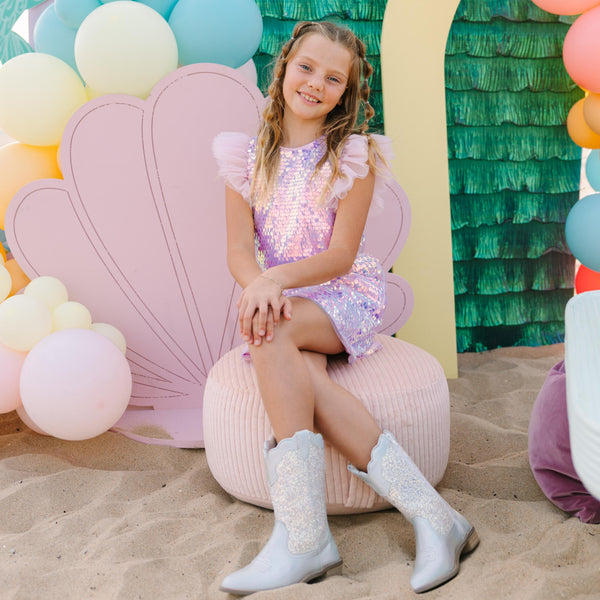 Young girl in a colorful dress sitting on a pink shell-shaped chair with a mermaid-themed backdrop.