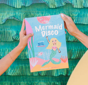 Book titled 'Mermaid Disco' held against a teal wave-patterned background