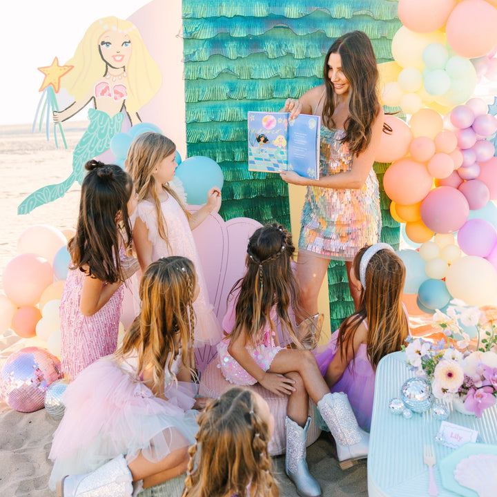 Woman with children at a mermaid-themed birthday party with balloons and a backdrop.