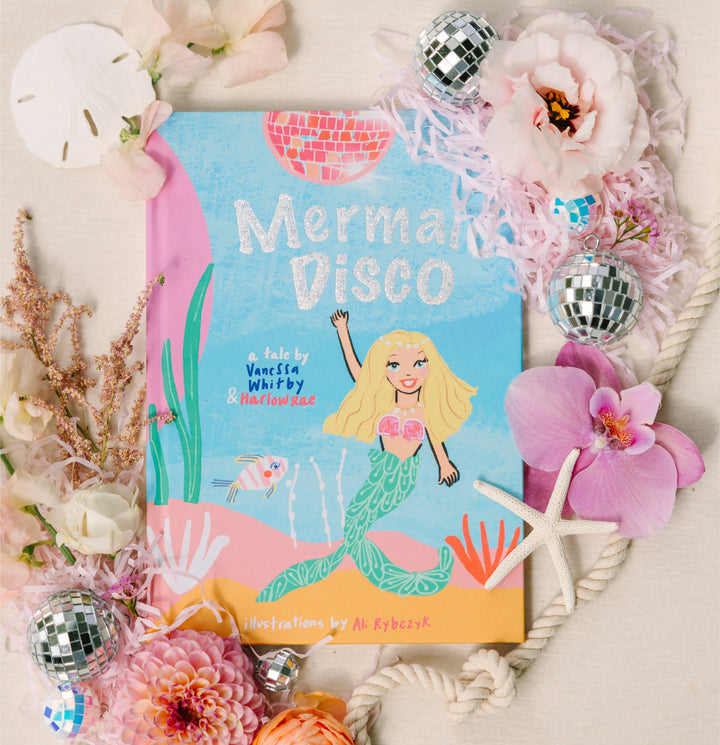 Book titled 'Mermaid Disco' surrounded by flowers and decorative elements on a light background