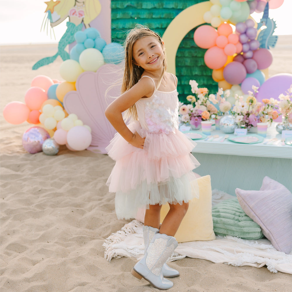 Young girl in a pink dress standing in front of a colorful balloon arch and decorated table.
