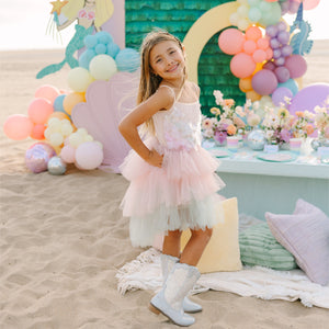 Young girl in a pink dress standing in front of a colorful balloon arch and decorated table.