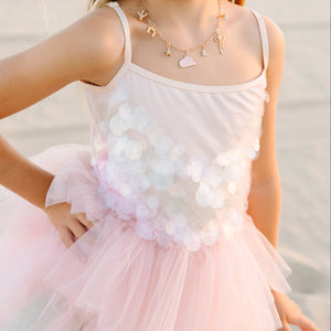 Young girl in a pink dress with floral details on a beach.