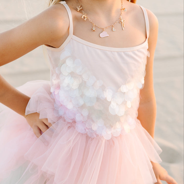 Young girl in a pink dress with floral details on a beach.