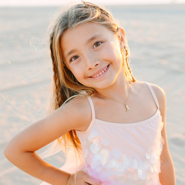 Young girl in a pink dress standing on a beach with a soft focus background