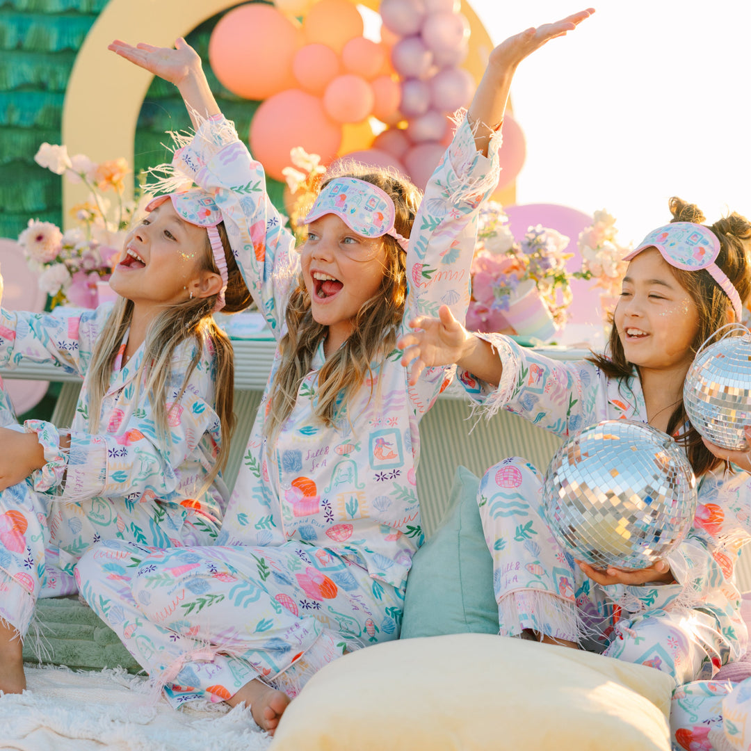Children in pajamas with decorative headbands and balloons, celebrating a birthday.