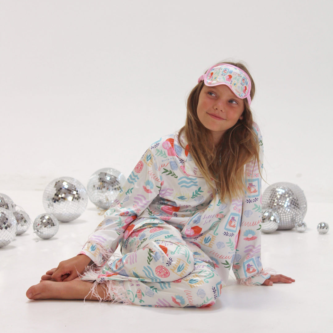 Girl wearing colorful pajamas and an eyemask, sitting on a white background with disco balls.