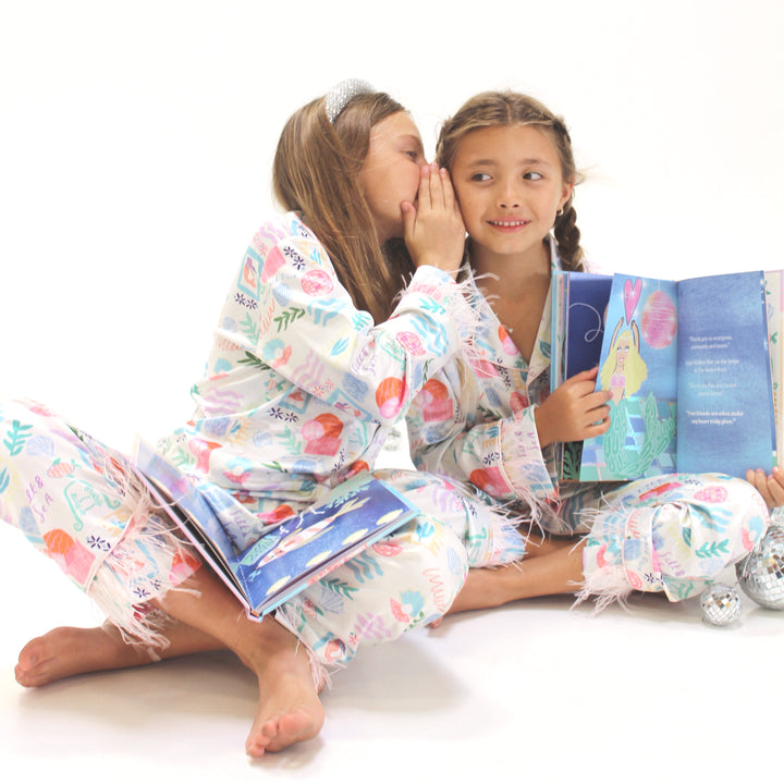 Two children in pajamas sitting on a white floor, reading books.