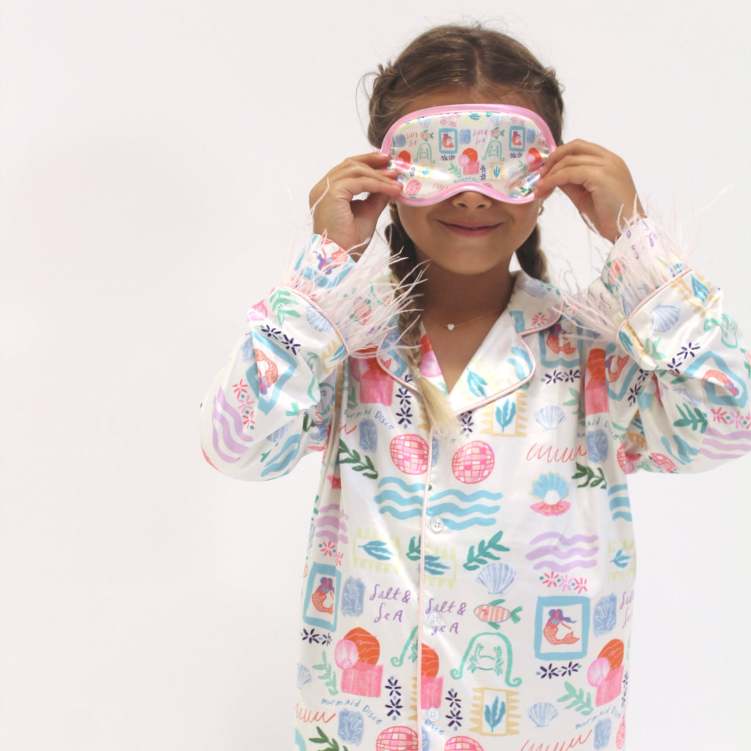 Child wearing a colorful pajama and matching sleep mask on a white background