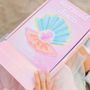 Pink box with mermaid design and text, held by a hand.