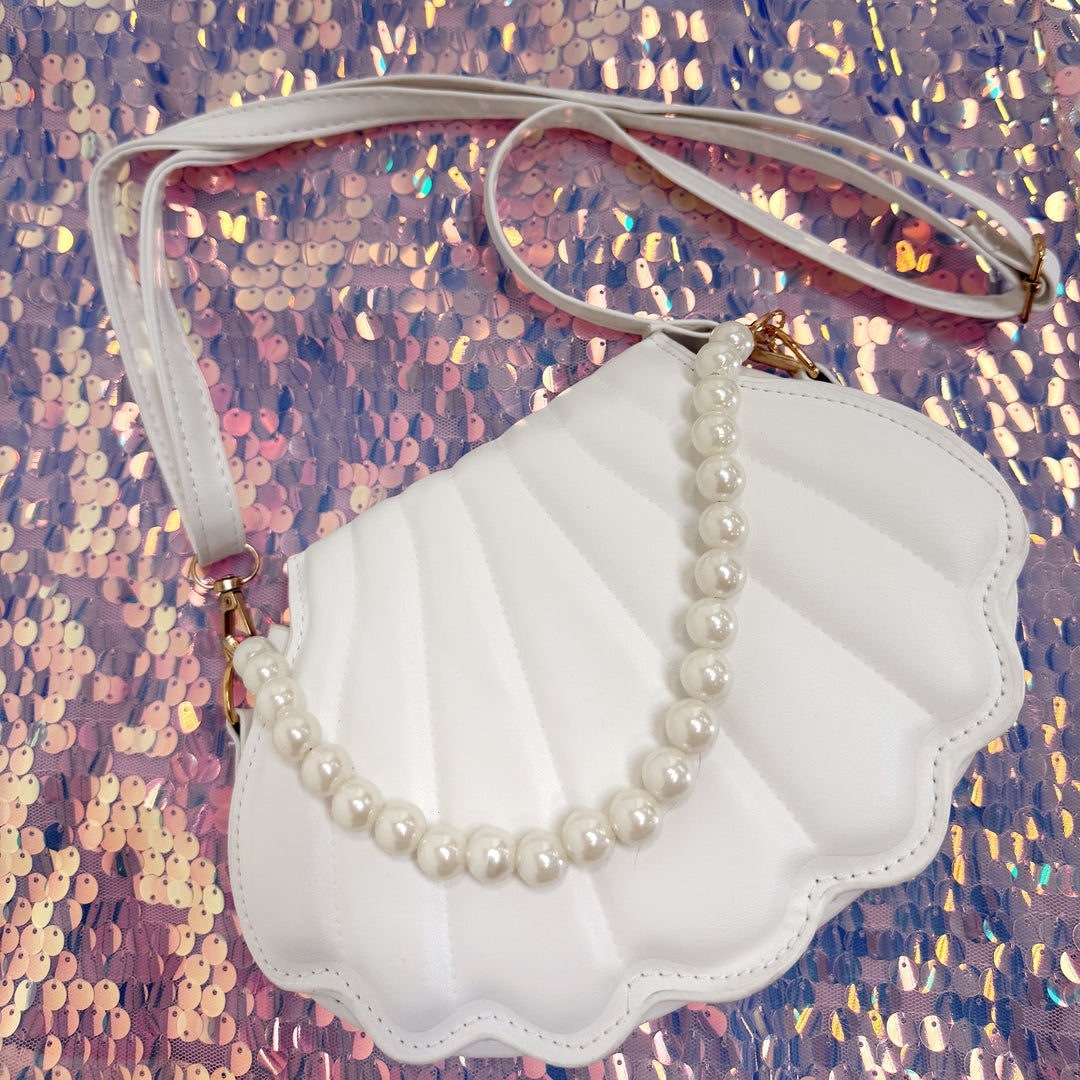 Shell-shaped handbag with a pearl necklace on a glittery pink background