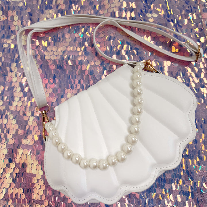 Shell-shaped handbag with a pearl necklace on a glittery pink background
