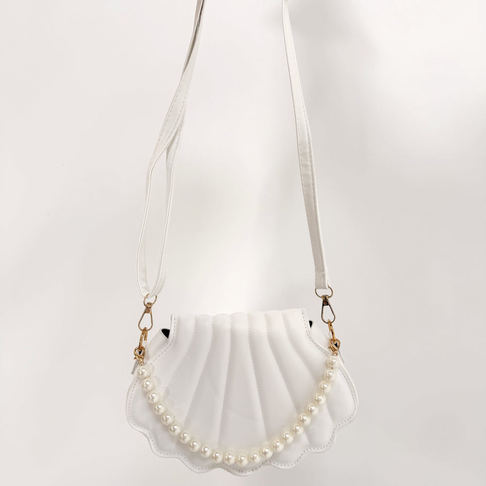 Shell-shaped handbag with pearl details held by a person on a white background