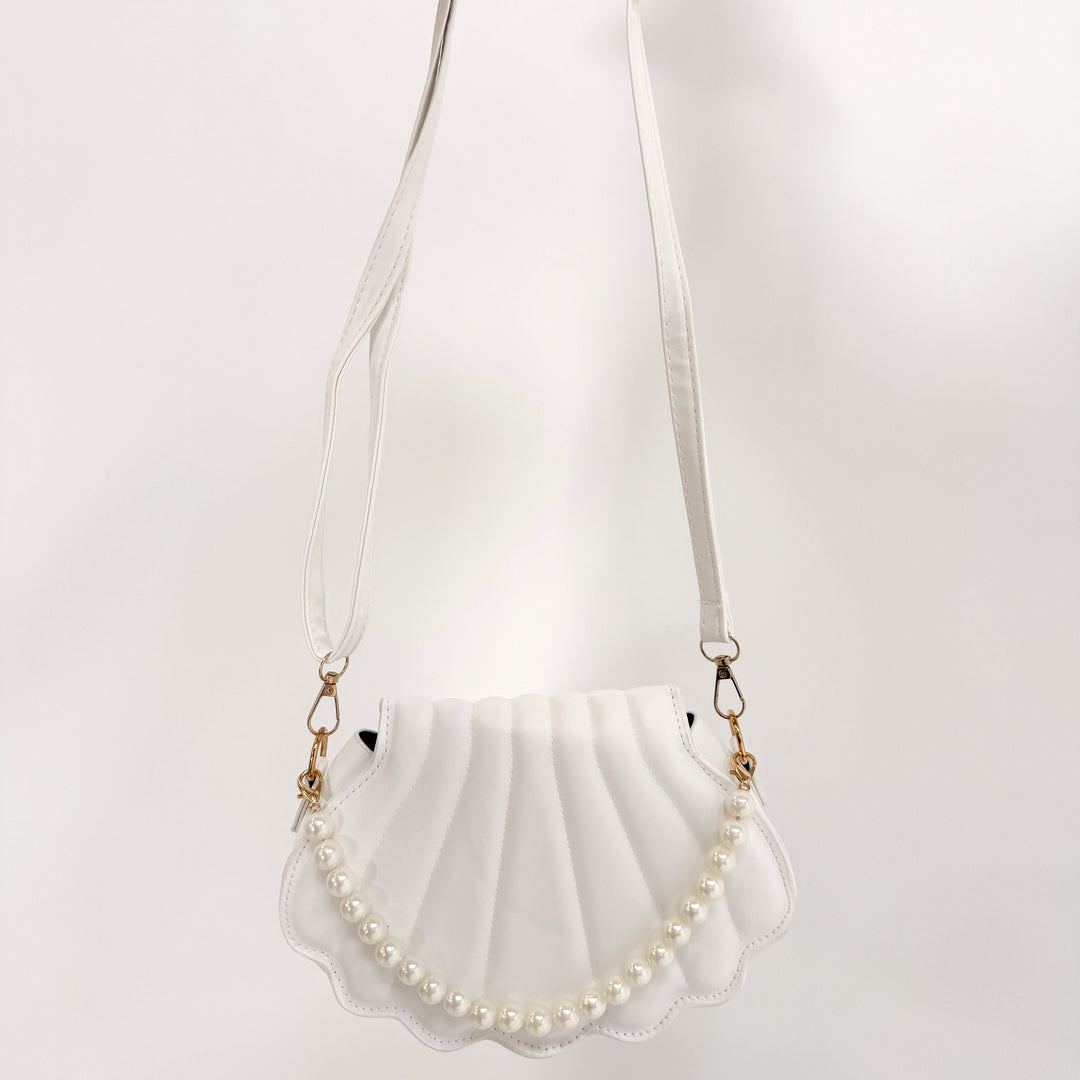 Shell-shaped handbag with pearl details held by a person on a white background