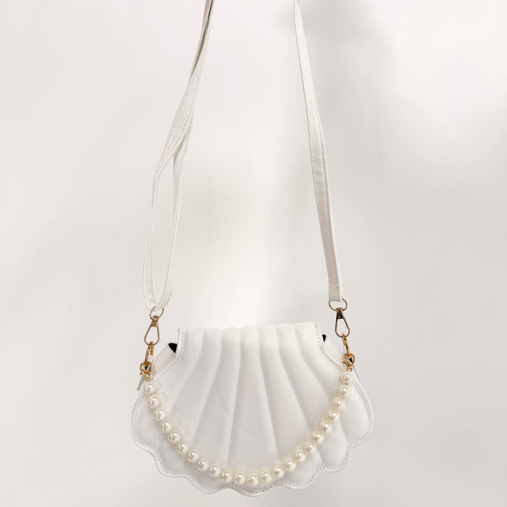 Shell-shaped handbag with pearl details held by a person on a white background