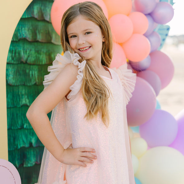 Young girl in a pink dress standing in front of colorful balloons and a green arch.